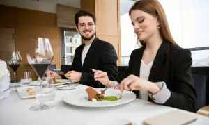 Elegancki strój na kolację do restauracji. Para w garniturach delektuje się wykwintnym deserem przy kieliszkach czerwonego wina.