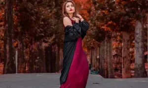 Elegancka kobieta w bordowej sukience i czarnym narzutce, idealne połączenie, które podpowiada, jakie dodatki do bordowej sukienki wybrać na jesienny spacer.