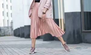 Kobieca stylizacja: pudrowy różowy żakiet i plisowana spódnica. Jakie buty do plisowanej spódnicy? Sneakersy w tym samym kolorze to strzał w dziesiątkę!