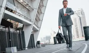 Elegancki garnitur i trampki na wesele – młody mężczyzna sprawdza zegarek, idąc z torbą obok nowoczesnego budynku.