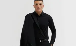 Mężczyzna w czarnym garniturze, z marynarką na ramieniu. Elegancki, czarny pasek do garnituru podkreśla jego styl.
