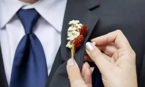 Dłoń przypina do marynarki elegancki kwiat w butonierce, dodając stylizacji uroku.