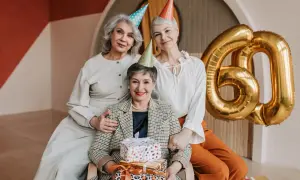 Eleganckie stylizacje na urodziny w lokalu. Trzy kobiety świętują 60. urodziny, otoczone prezentami i złotymi balonami.