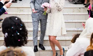 Eleganckie ślubne stylizacje pary młodej na schodach, obsypanej konfetti. Panna młoda w koronkowej sukience, pan młody w szarym garniturze.