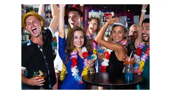 Grupa przyjaciół świętuje w klubie w stylu hawajskim, z kolorowymi girlandami i drinkami.
