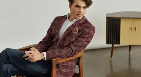 Elegancka marynarka w kratę do jeansów to idealny wybór na stylową stylizację. Mężczyzna siedzi na krześle, prezentując zestaw.
