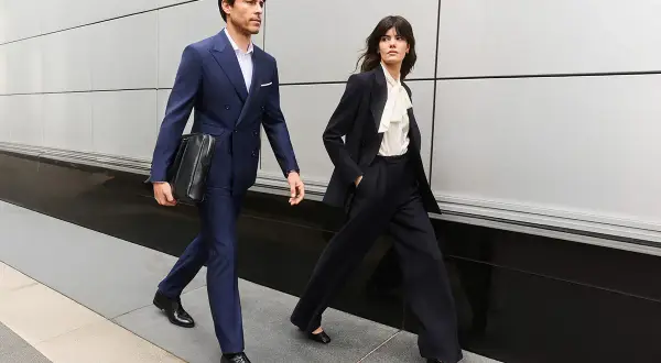 Para idą w eleganckim business attire, mężczyzna w granatowym garniturze, kobieta w czarnym.