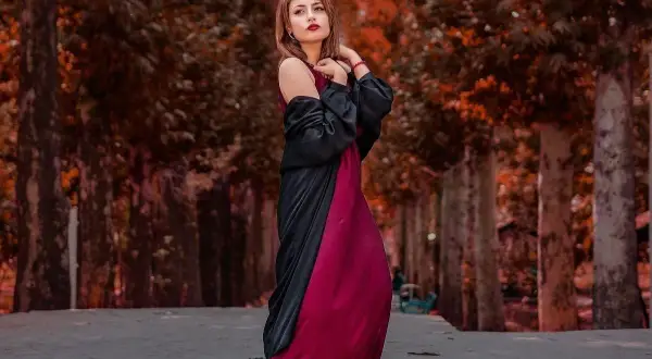 Elegancka kobieta w bordowej sukience i czarnym narzutce, idealne połączenie, które podpowiada, jakie dodatki do bordowej sukienki wybrać na jesienny spacer.