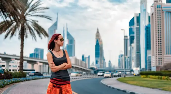 Turystka w Dubaju w pomarańczowej spódnicy i topie podziwia panoramę miasta.