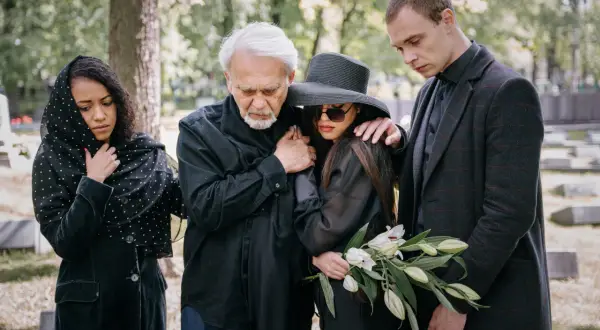 Smutna rodzina na cmentarzu. Elegancki ubiór damski na pogrzebie latem, z welurową marynarką i kapeluszem.