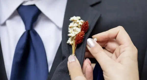 Dłoń przypina do marynarki elegancki kwiat w butonierce, dodając stylizacji uroku.