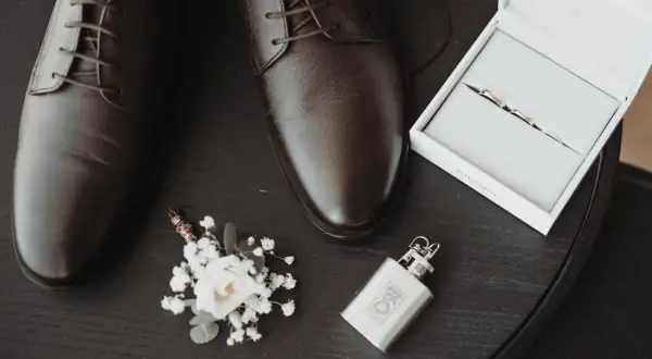 Eleganckie, brązowe oksfordy – jeden z klasycznych rodzajów butów męskich. Obok butonierka, obrączki i piersiówka.