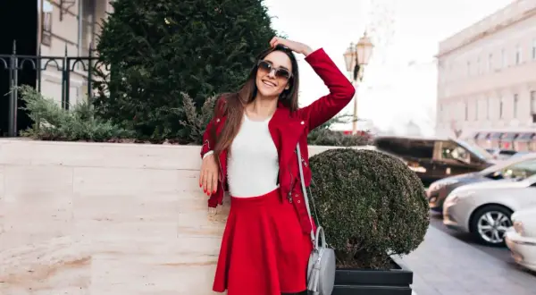 Elegancka stylizacja na mecz do strefy VIP: czerwona ramoneska, biały sweterek, krótka spódniczka i szara torebka.