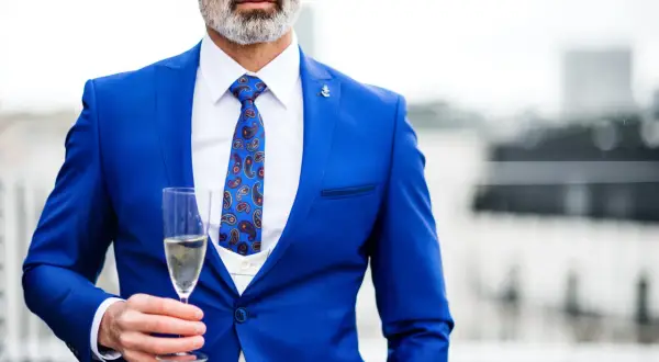 Elegancki mężczyzna w niebieskim stroju koktajlowym z wzorzystym krawatem trzyma kieliszek szampana.