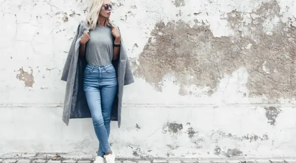 Modelka w jasnych jeansach skinny i szarym płaszczu. Dowiedz się, jakie jeansy do jakiej figury pasują najlepiej.