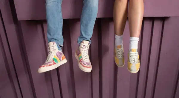 Kolorowe buty sneakersy i żółte, klasyczne sneakersy na nogach siedzących osób.