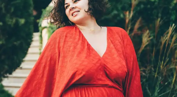Uśmiechnięta kobieta w czerwonej sukni, jakby była figurą jabłko gwiazdy, otoczona zielenią.