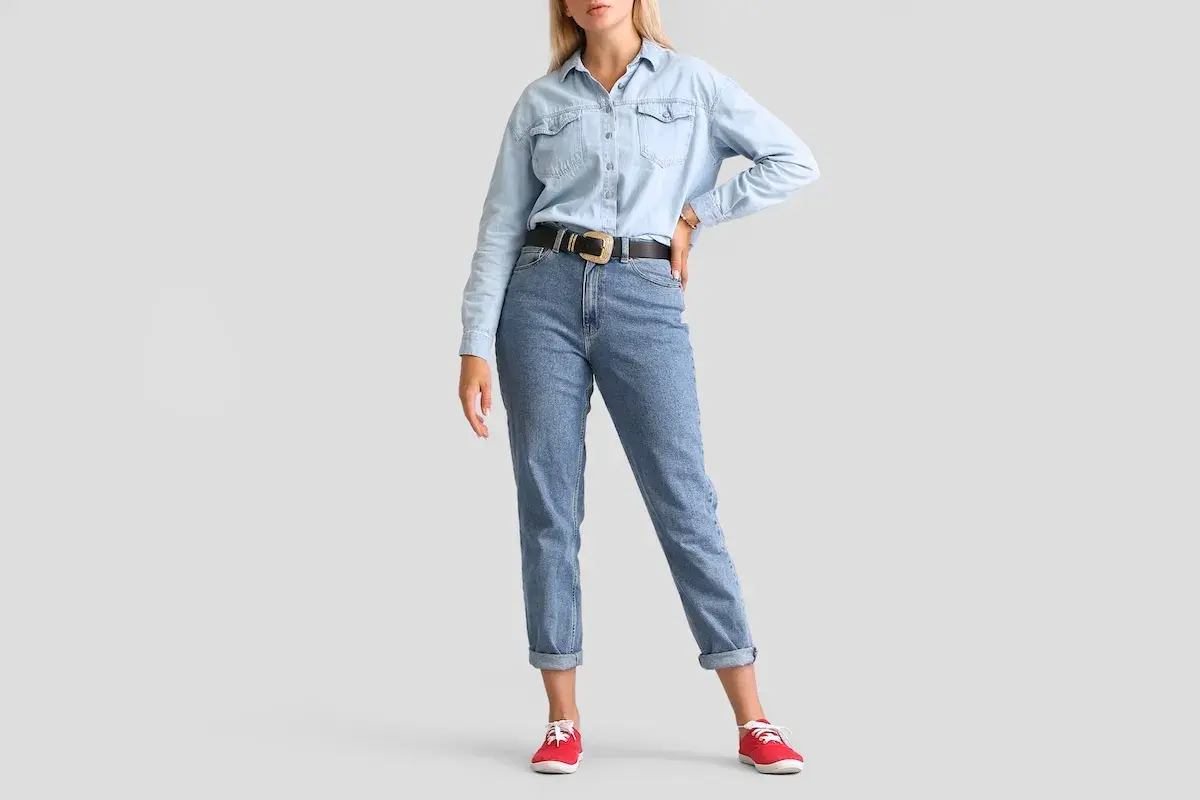 Modelka w jasnych jeansach z podwiniętymi nogawkami i jeansowej koszuli. Idealne jeansy dla niskiej osoby, które optycznie wydłużają nogi.