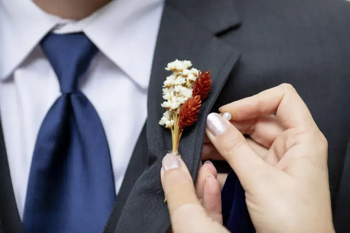 Dłoń przypina do marynarki elegancki kwiat w butonierce, dodając stylizacji uroku.