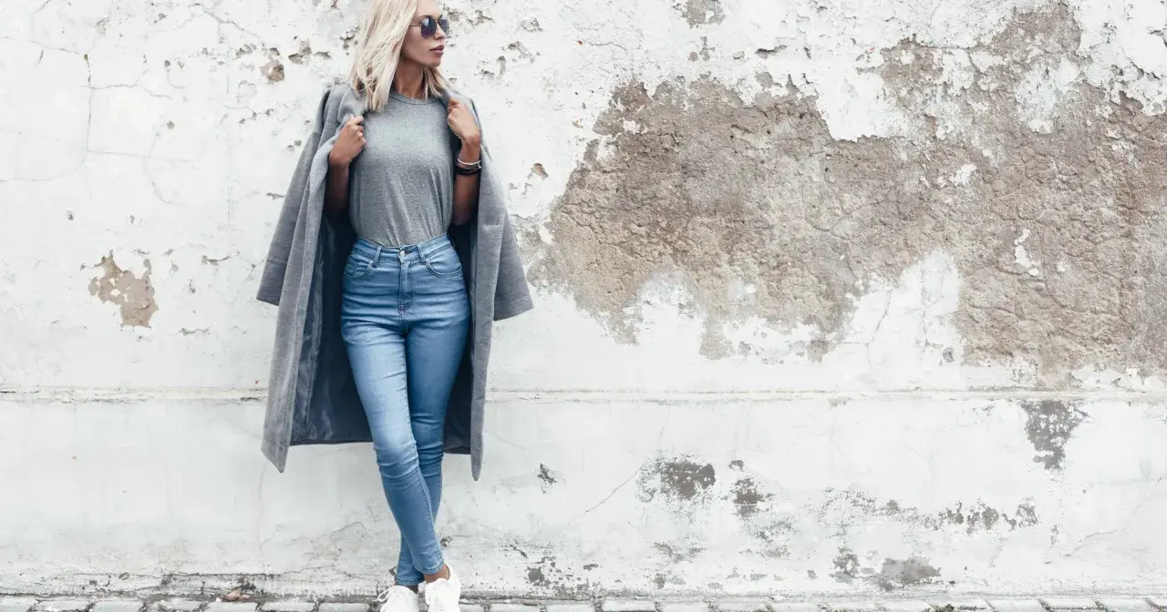 Modelka w jasnych jeansach skinny i szarym płaszczu. Dowiedz się, jakie jeansy do jakiej figury pasują najlepiej.