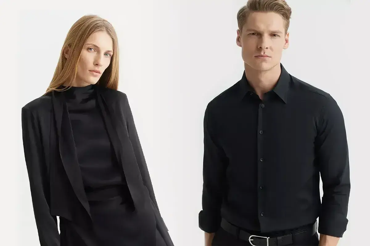 Elegancka kobieta w czarnej bluzce i marynarce, obok mężczyzna w czarnej koszuli. Jaka koszula do czarnych spodni? Klasyka zawsze się obroni.