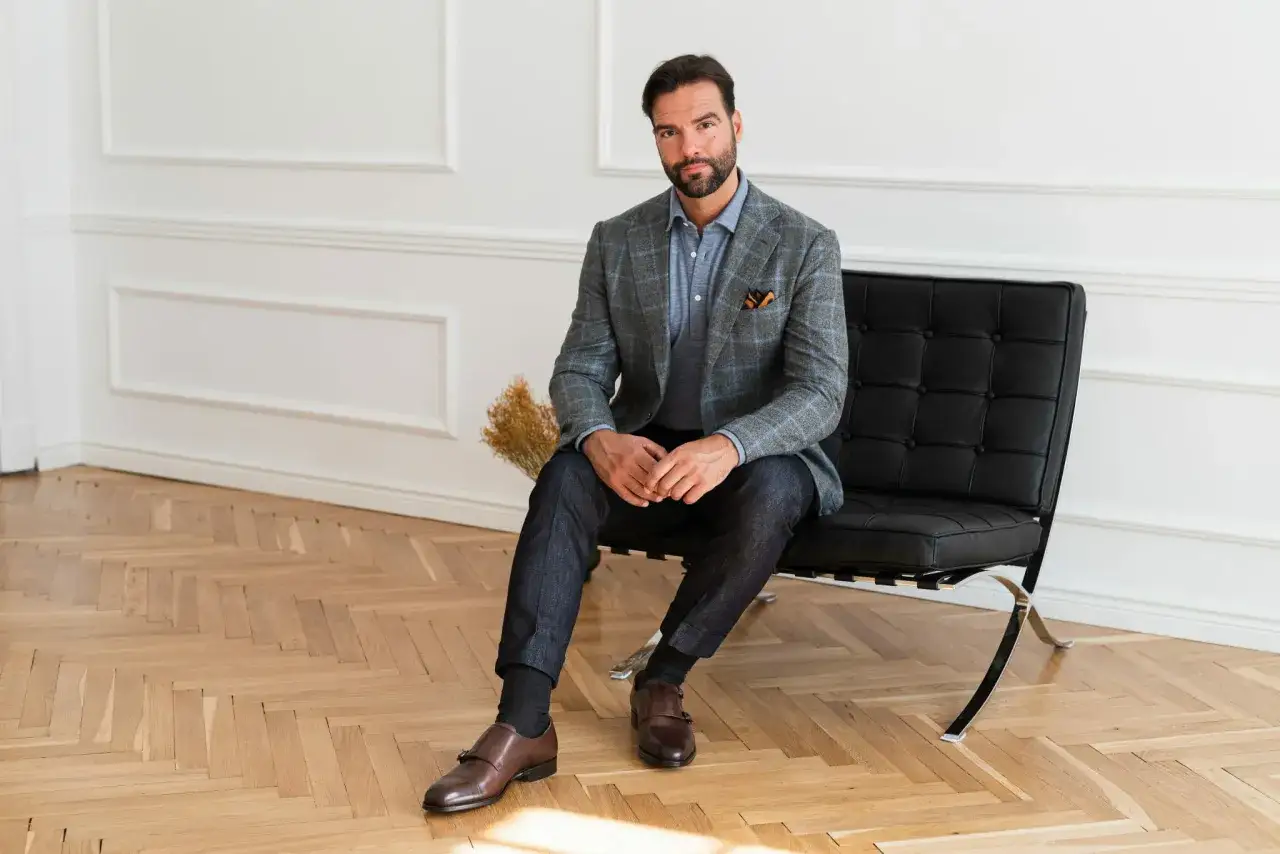 Elegancka, kraciasta marynarka do jeansów to idealny wybór. Mężczyzna w stylowym zestawie siedzi na czarnym fotelu.