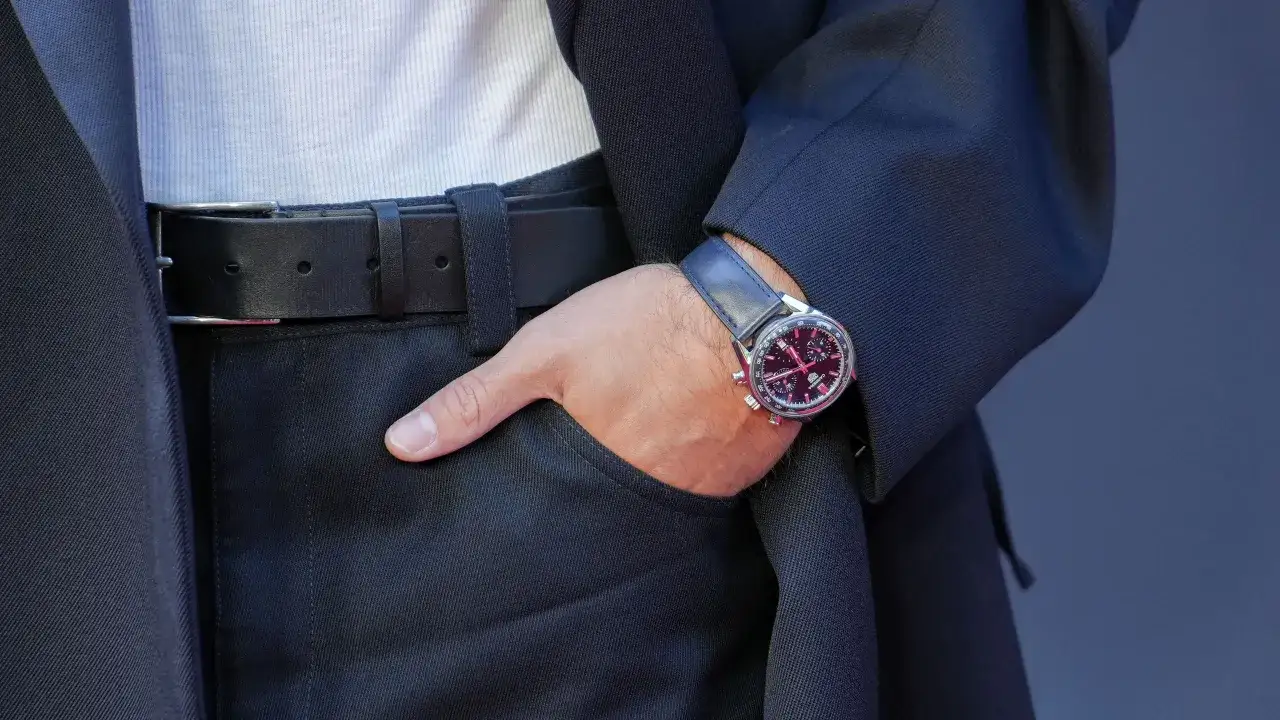 Elegancki mężczyzna w garniturze, z ręką w kieszeni, pokazuje, jak wysoko nosić zegarek. Klasyka stylu.