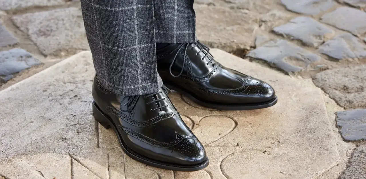 Eleganckie, czarne, lakierowane oksfordy z ażurowymi zdobieniami to idealne buty do czarnego garnituru, podkreślające styl.
