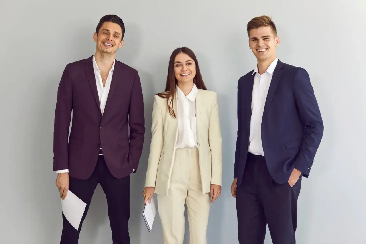 Trzy osoby w eleganckim, biznesowym ubiorze na rozmowę o pracę. Uśmiechnięci, pewni siebie kandydaci.